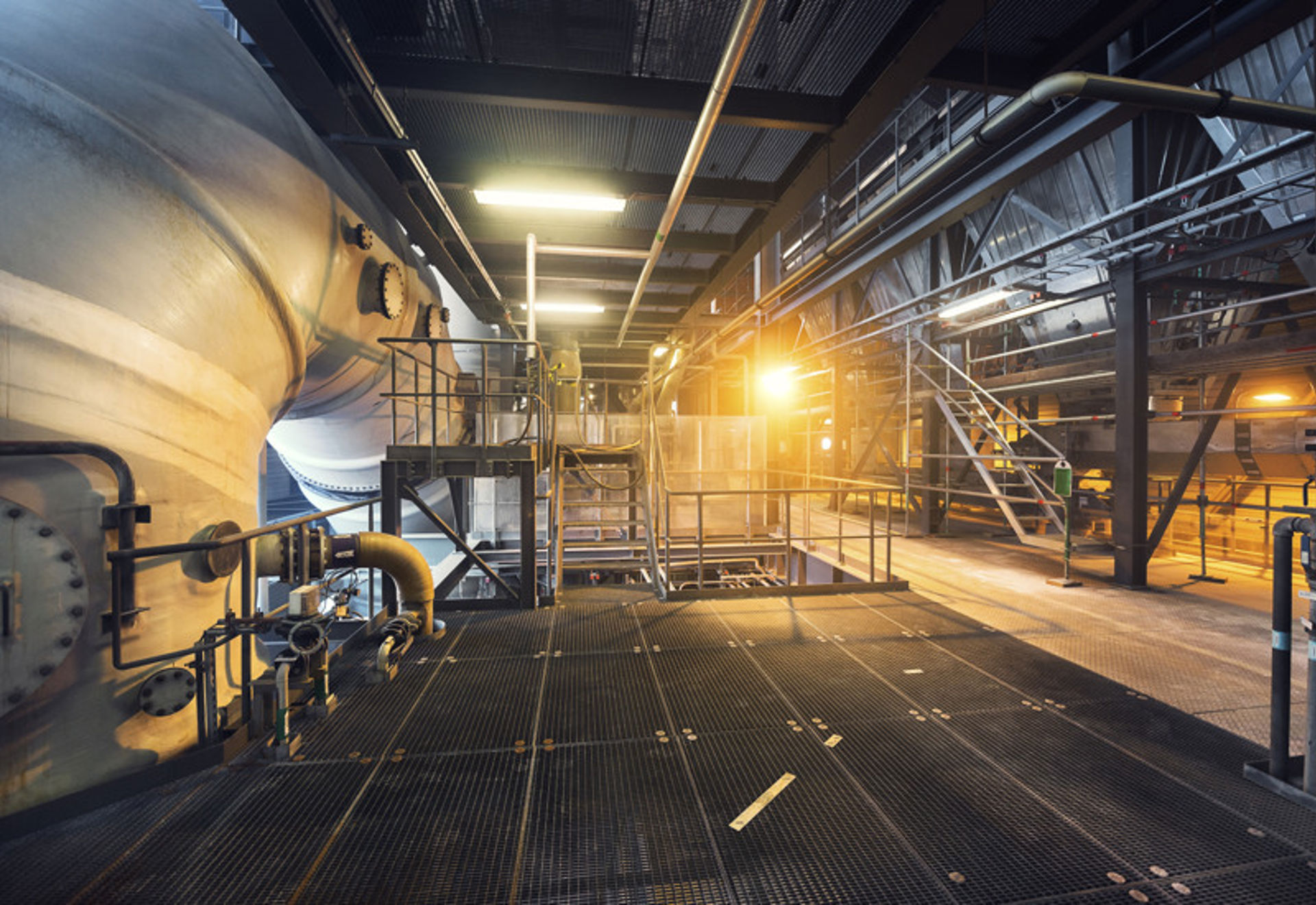 Industrimiljö i motljus. Stålrör, staket och lampor ger en robust känsla.